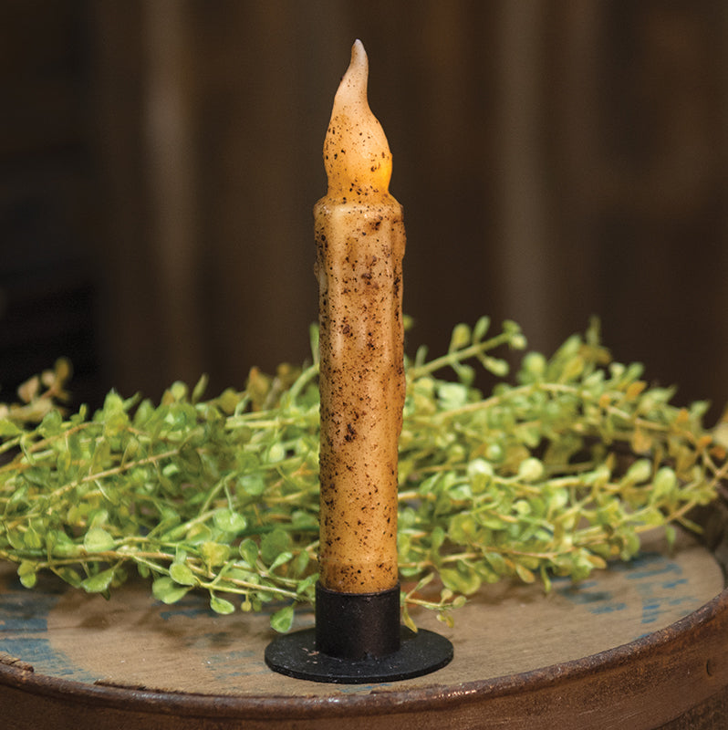 Circle taper holder in black holding a battery operated mustard taper with greenery in the background