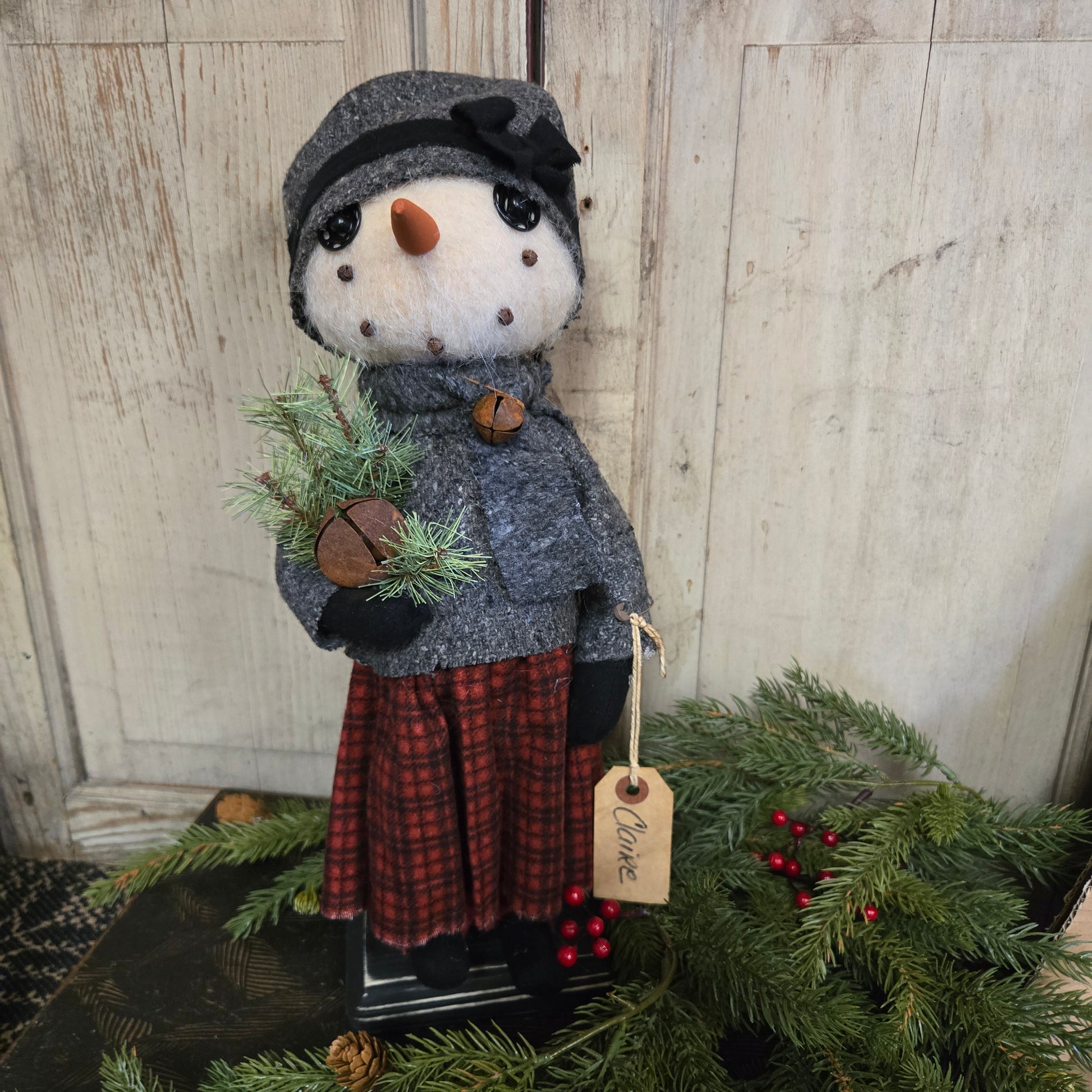 Decorative snowman with a tag labeled 'Claire' next to a wreath on a wooden surface