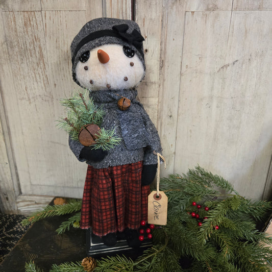 Decorative snowman with a tag labeled 'Claire' next to a wreath on a wooden surface