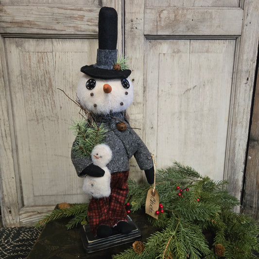 Decorative snowman figure with a snowman next to a Christmas tree on a wooden floor.