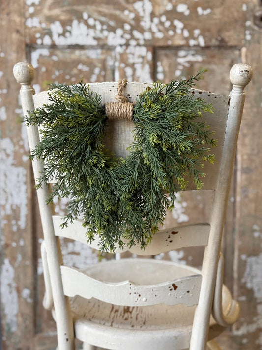Green wreath hanging on a white wooden chair against a rustic wooden wall.