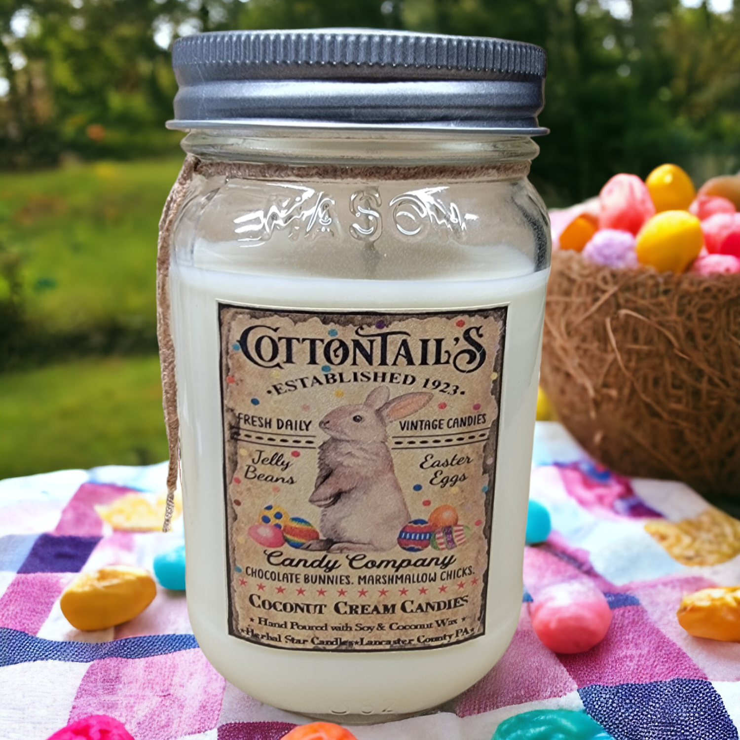 A mason jar candle with a label that reads 'Cottontail's Established 1921 - Vintage Candy Company', featuring an illustration of a rabbit with candy canes, placed on a picnic blanket with Easter eggs and candy canes around.