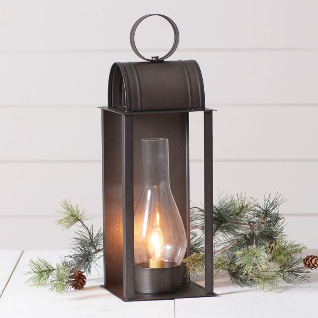 Decorative lantern with a lit candle inside, surrounded by greenery on a white background