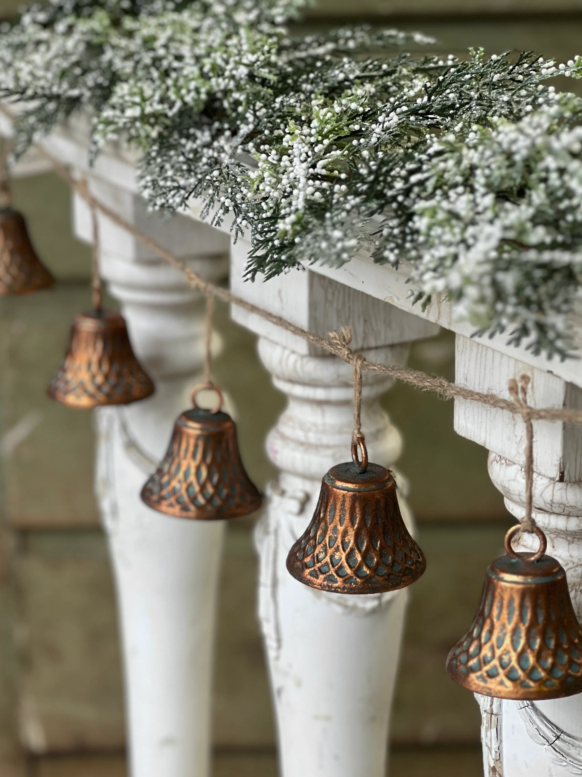 A garland of copper-toned bells with a geometric pattern hung against a white backdrop, resembling holiday decorations.