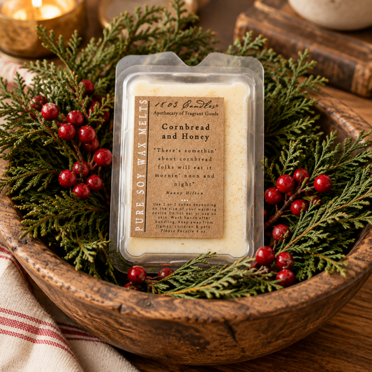 A packaged soy wax melt sits in a rustic wooden bowl surrounded by green pine branches and red berries. The product label reads '15 1/3 Barrel Co.