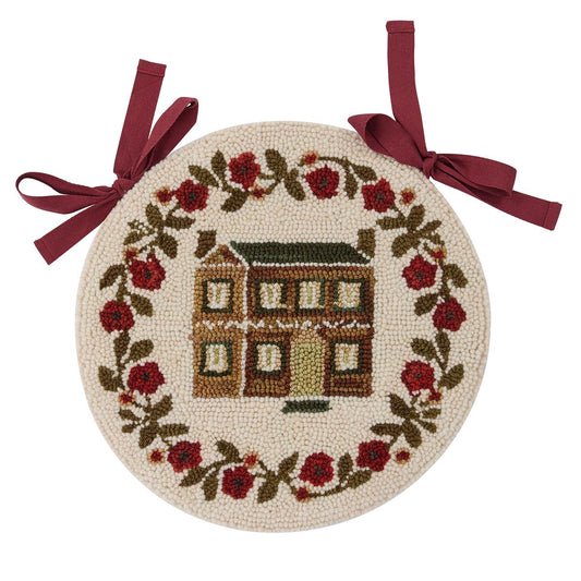Decorative round mat with embroidered house and floral design, tied with ribbons on a white background.