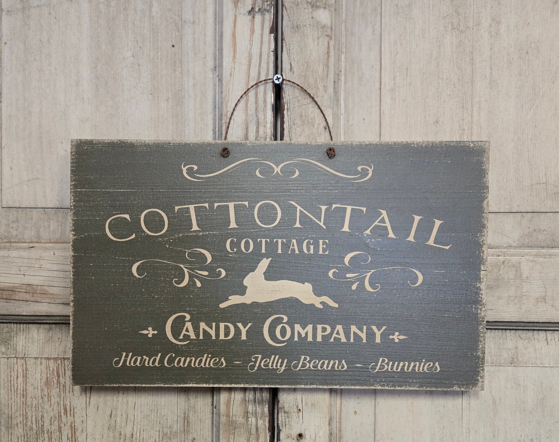 Wooden sign with 'Cottontail Cottage Candy Company' text and rabbit illustration on a wooden background