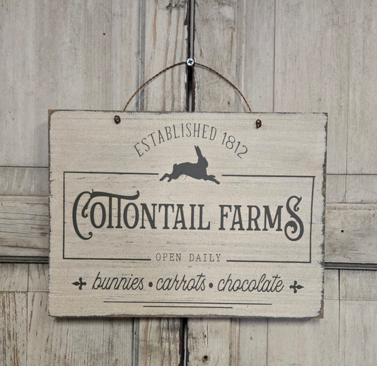 Wooden sign with 'Cottontail Farms' text and rabbit illustration on a wooden background