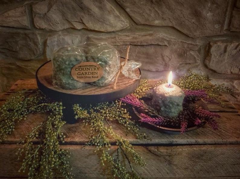 A votive candle with a citrus fragrance, displayed in a setting that includes a second votive in its packaging, surrounded by decorative plants on a wooden surface.
