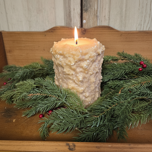Decorative candle with a flame surrounded by greenery on a wooden surface