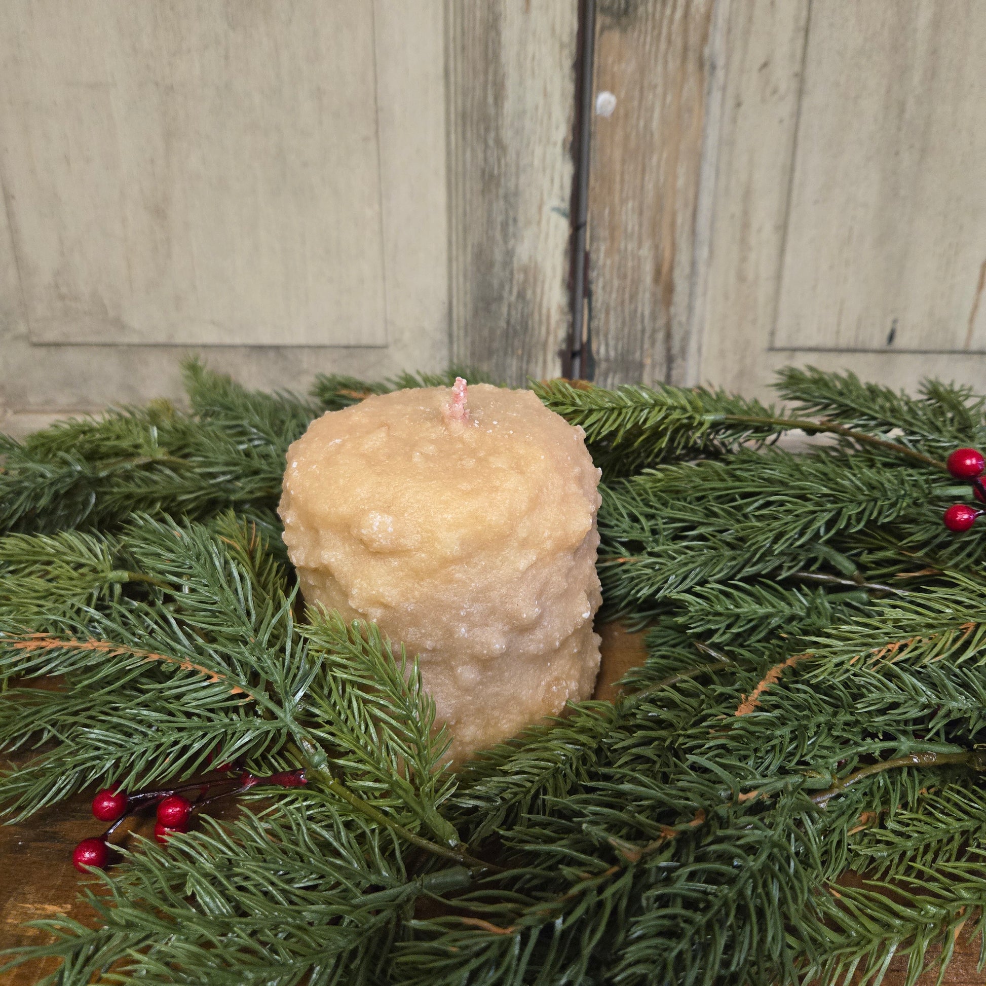 A cream colored candle with a bumpy texture surrounded by Christmas greenery