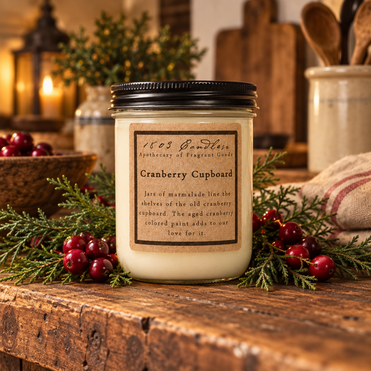 A jar candle labeled 'Cranberry Cupboard' by 165 Candlehouse, styled on a rustic wooden table with greenery and cranberries in a cozy, warm setting.