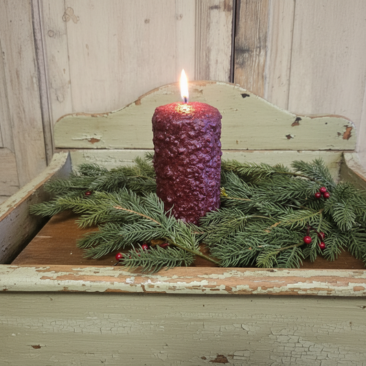 Purple candle with greenery on a rustic wooden surface
