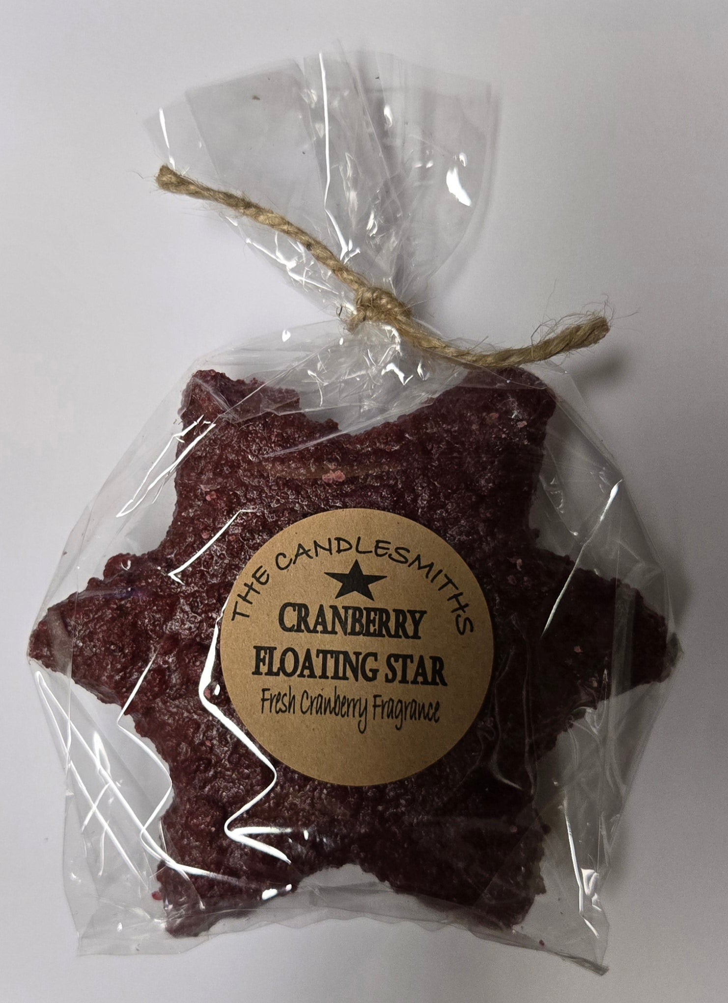 A cranberry-colored large star-shaped floating candle, packaged in clear wrapping with a label and a string tied to the top.