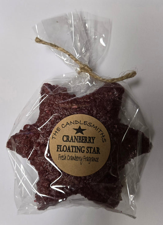 A cranberry-colored large star-shaped floating candle, packaged in clear wrapping with a label and a string tied to the top.