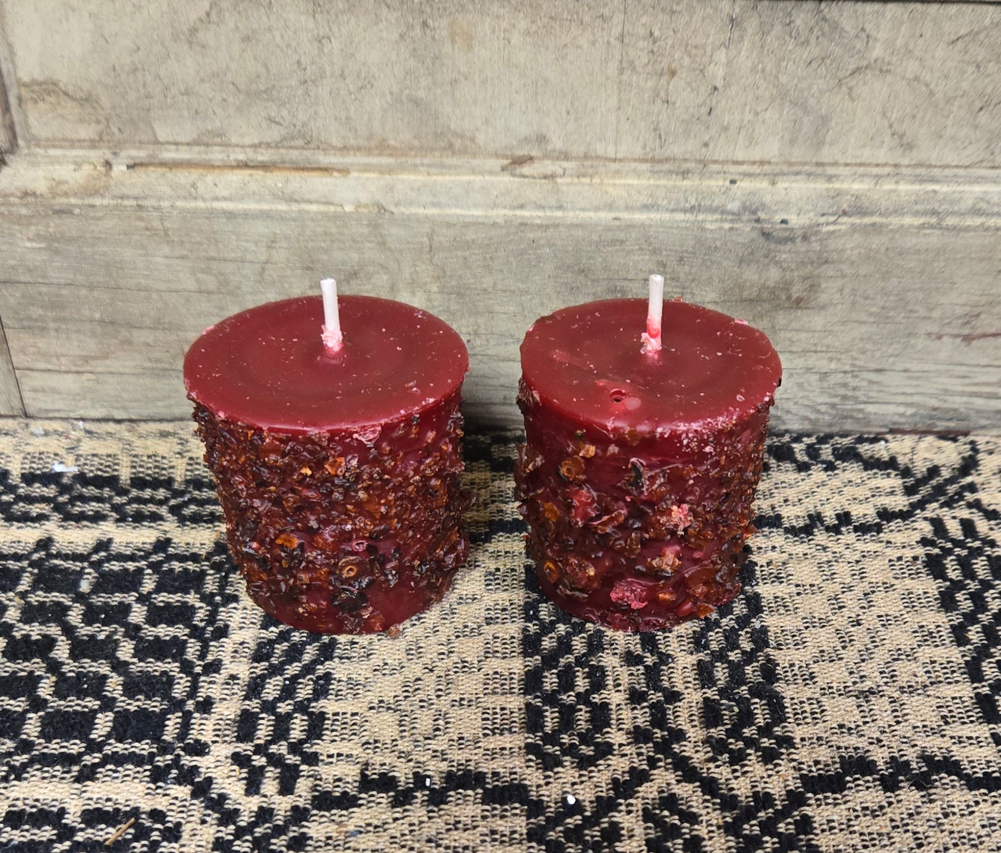 Two cylindrical cranberry-scented votive candles placed on a textured surface.