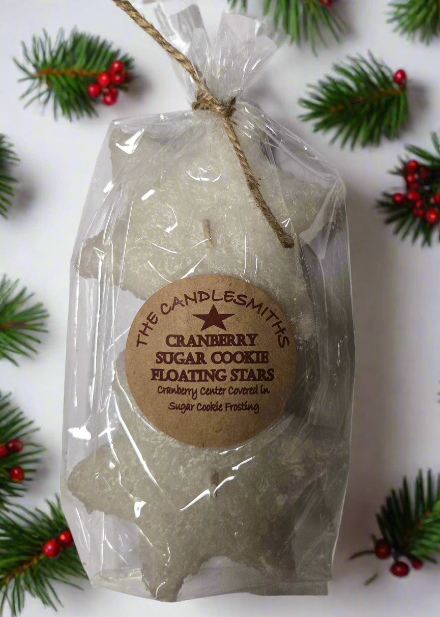 Two white floating candles designed to look like stars, packaged in clear wrapping with a label surrounded by pine sprigs.