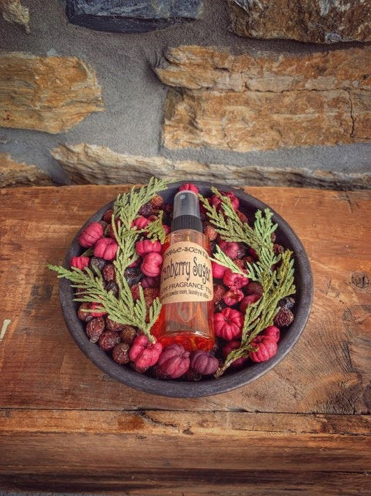 Metal pan filled with cranberry colored pods and sprigs of pine with a bottle of scented oil