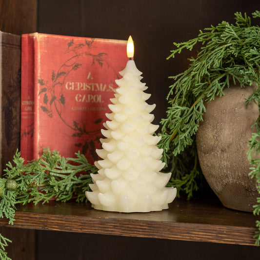 Decorative candle shaped like a Christmas tree on a shelf with a book and greenery.