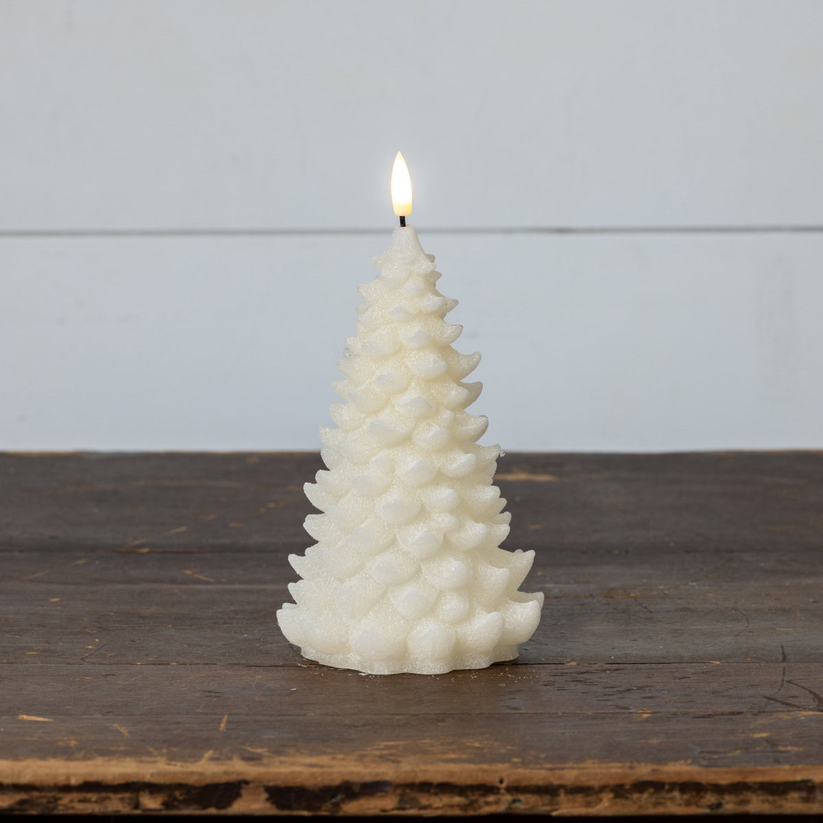 White textured candle shaped like a Christmas tree on a wooden surface with a light gray background