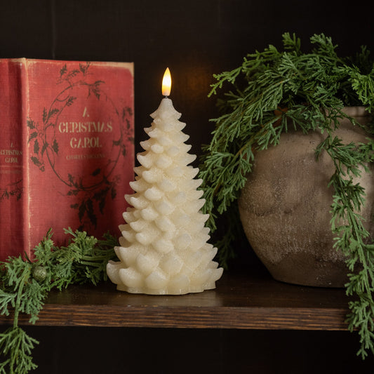 Decorative candle shaped like a Christmas tree on a shelf with a book and plant.