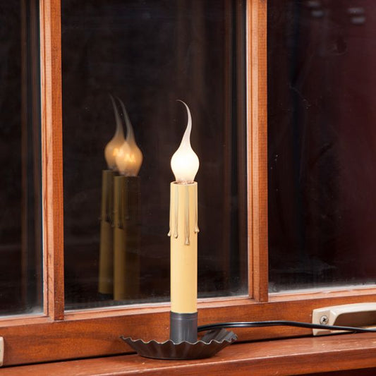 A black window sill light with a candle appearance placed on a windowsill, reflecting light on the window's surface.