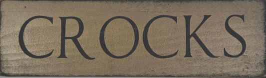 Rectangular wooden sign with 'CROCKS' text on a gray background