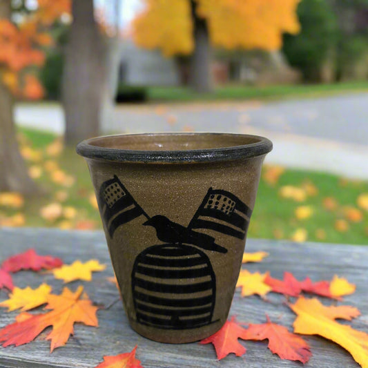 Decorative pot with a bird design on a wooden surface with autumn leaves