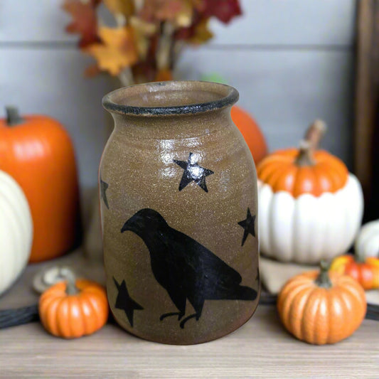 Decorative jar with crow and star design surrounded by pumpkins