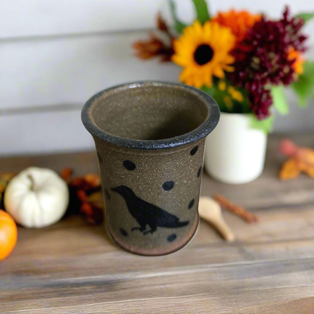 Ceramic cup with a bird design on a wooden surface with autumn decorations.
