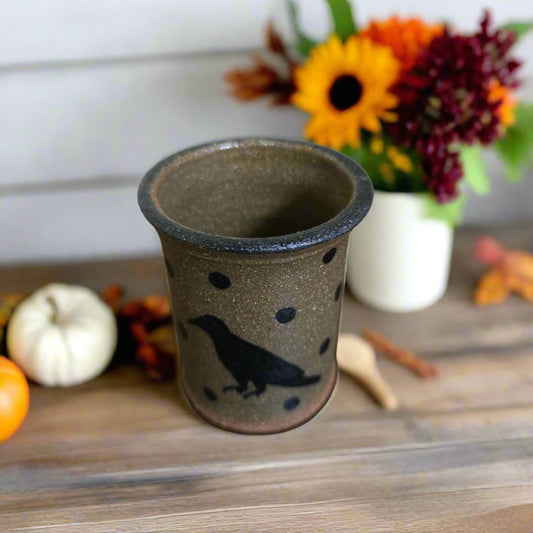 Ceramic cup with a bird design on a wooden surface with autumn decorations.