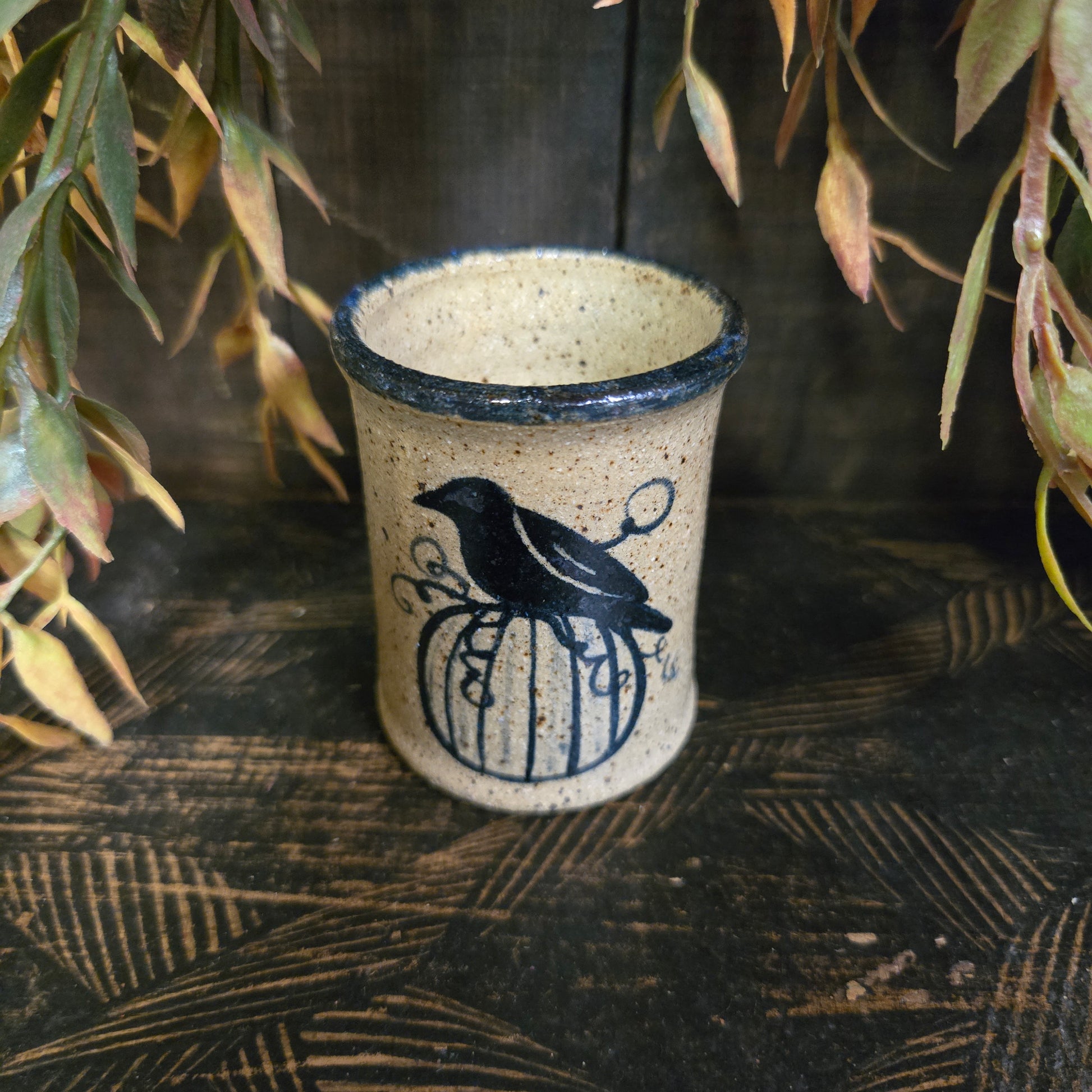 Ceramic cup with black design on a textured surface with plants