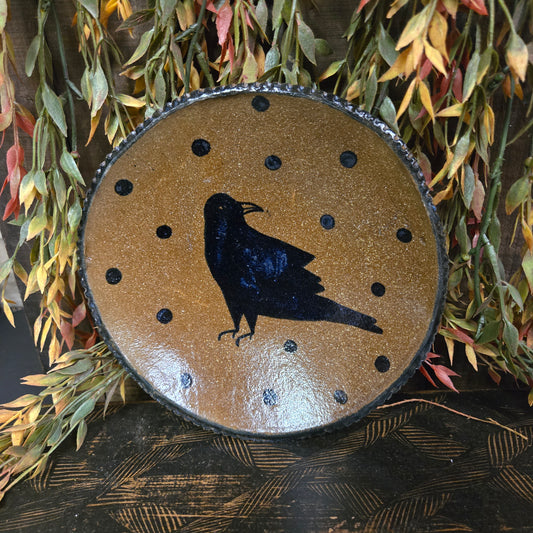 Round stoneware plate with black silhouette of a bird on a brown background, surrounded by autumn leaves.