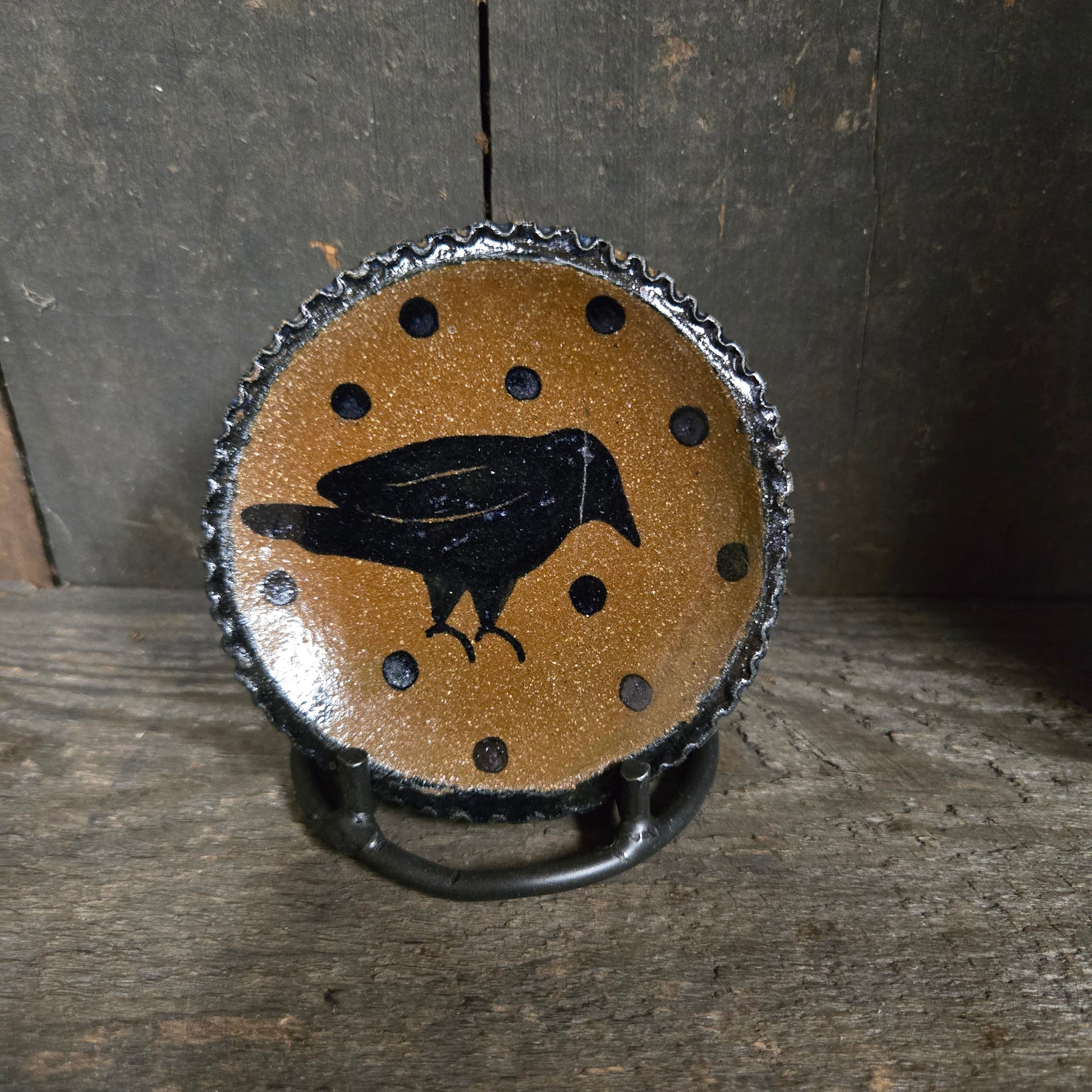 Decorative stoneware plate with a black bird silhouette on a brown background, placed on wooden surface.