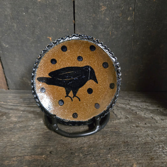 Decorative stoneware plate with a black bird silhouette on a brown background, placed on wooden surface.
