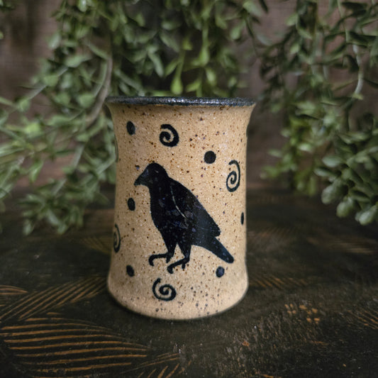 Miniature crock with a black bird design on a textured surface with greenery