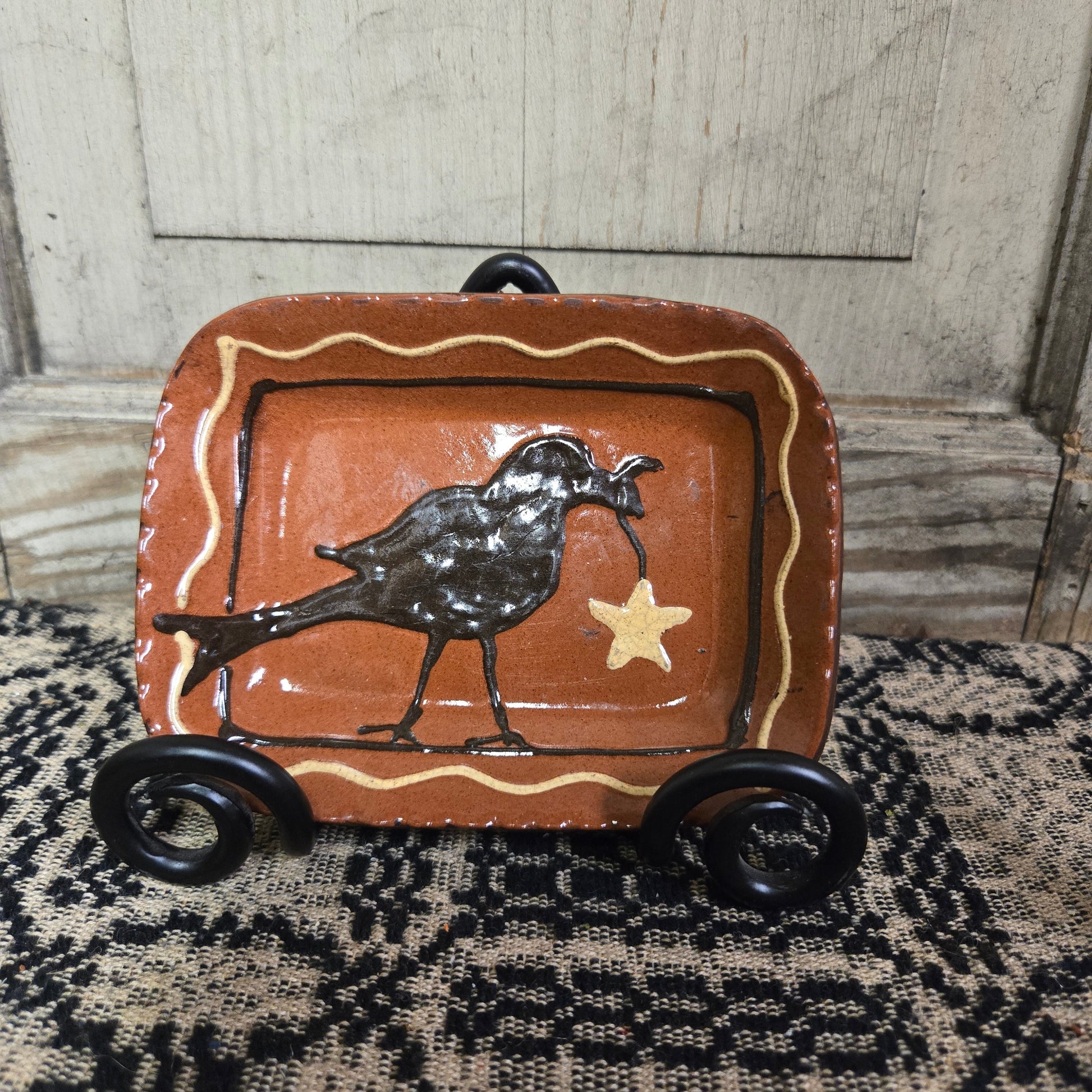 Small rectangular redware plate with a crow and a star hanging from its beak