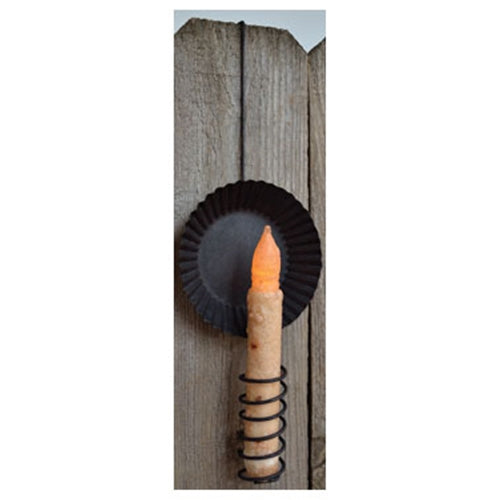 A black candle holder with a square-topped wire candle holder attached to a wooden door, with a fluted pan base designed to reflect light.