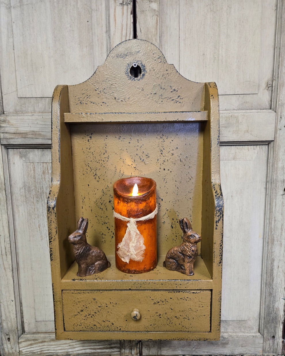 Decorative wall shelf with a candle and rabbit figurines against a wooden background