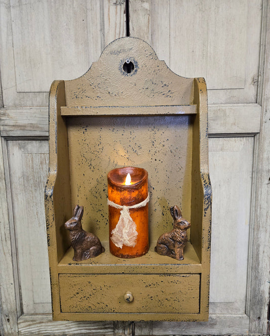 Decorative wall shelf with a candle and rabbit figurines against a wooden background