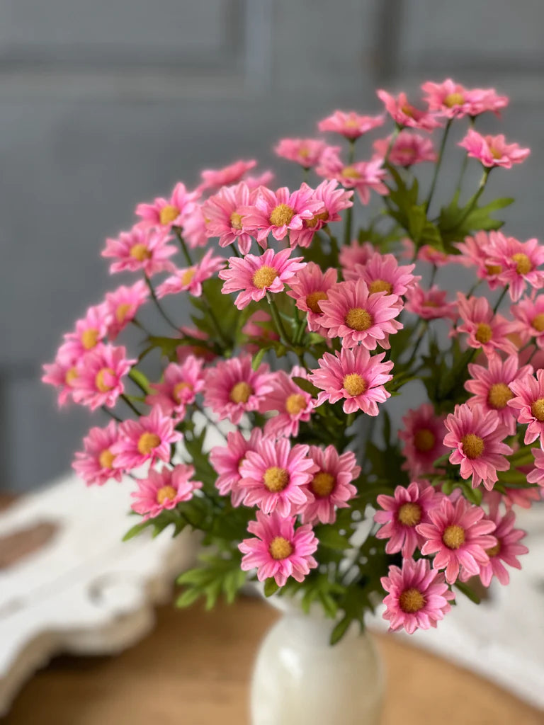 Bouquet of pink flowers in a white vase on a wooden surface with a gray background