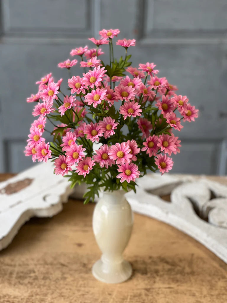 Bouquet of pink flowers in a white vase on a wooden surface with a gray wall background