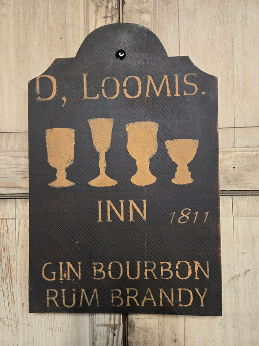 A rustic dark wood hanging sign for a Loomis Inn gin, bourbon, rum, and brandy, featuring gold lettering and four goblet silhouettes, shown against a light wood plank background.