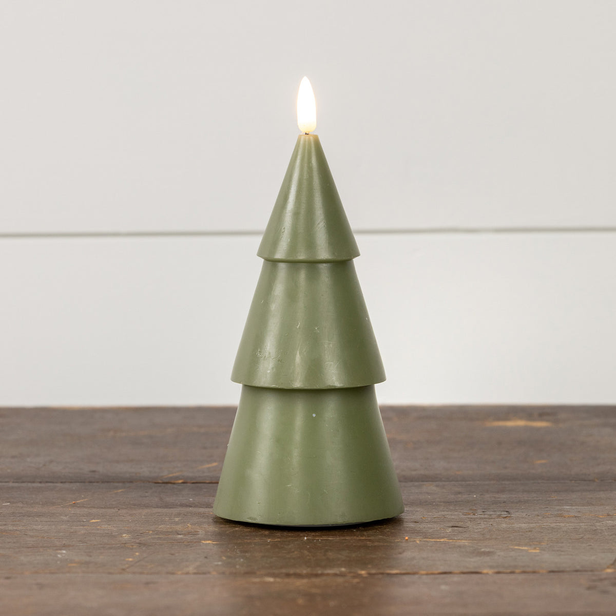 Green Christmas tree-shaped candle with a flame on a wooden surface and white background