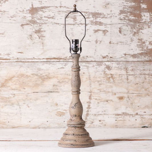 A beige, textured painted wood table lamp base with a black chisel base on top, standing against a wooden backdrop.