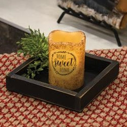 A distressed black wooden square candle box with a candle inside, placed on a textured surface. The box has a flat bottom and is freestanding.