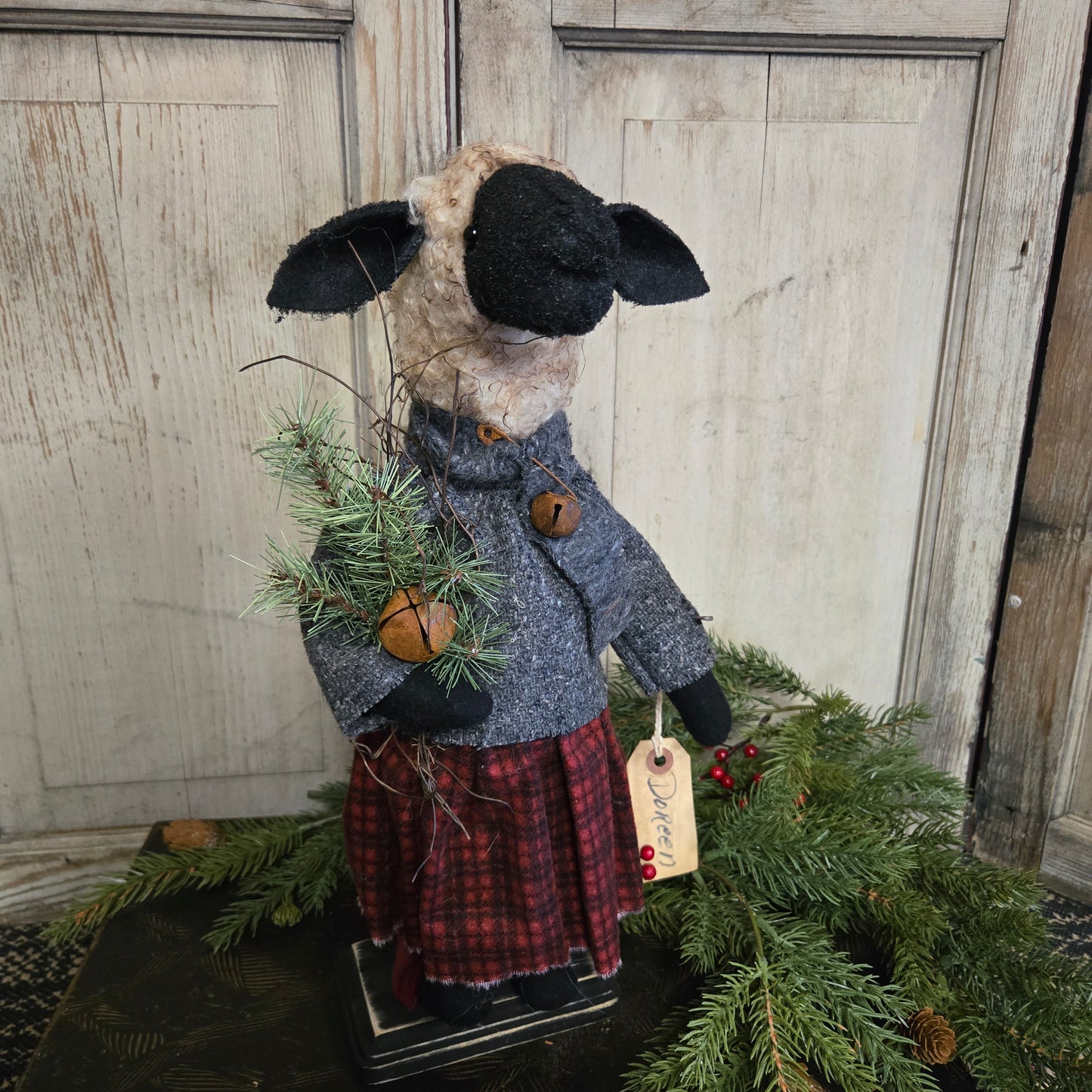 Decorative sheep figure with a plaid coat and black hat, standing next to a Christmas tree.