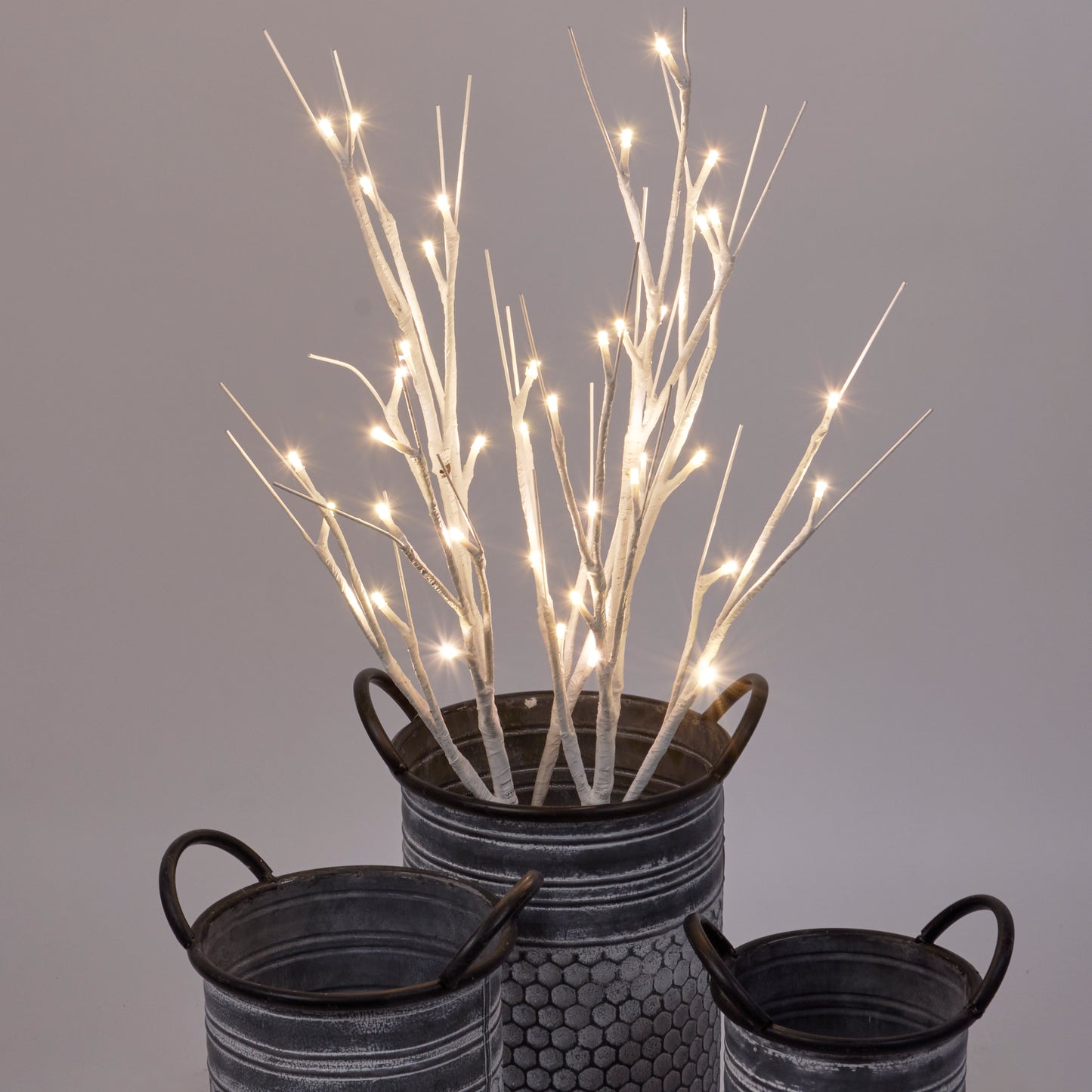 A pair of lighted white birch twigs displayed in a metal vase with handles, showcasing warm white LED lights.