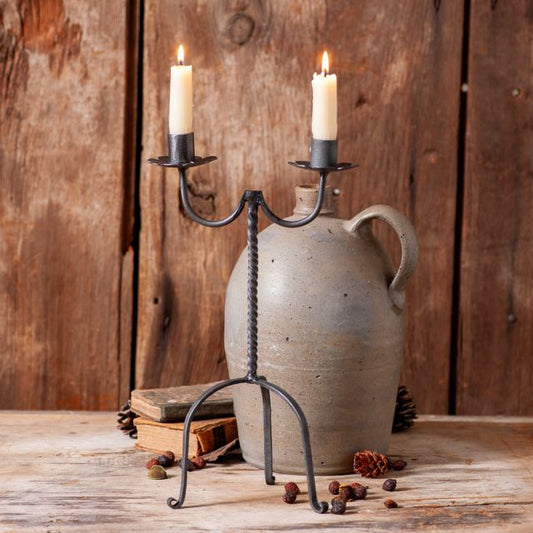 Wrought iron candleholder that holds two real or battery operated taper candles with jug in background