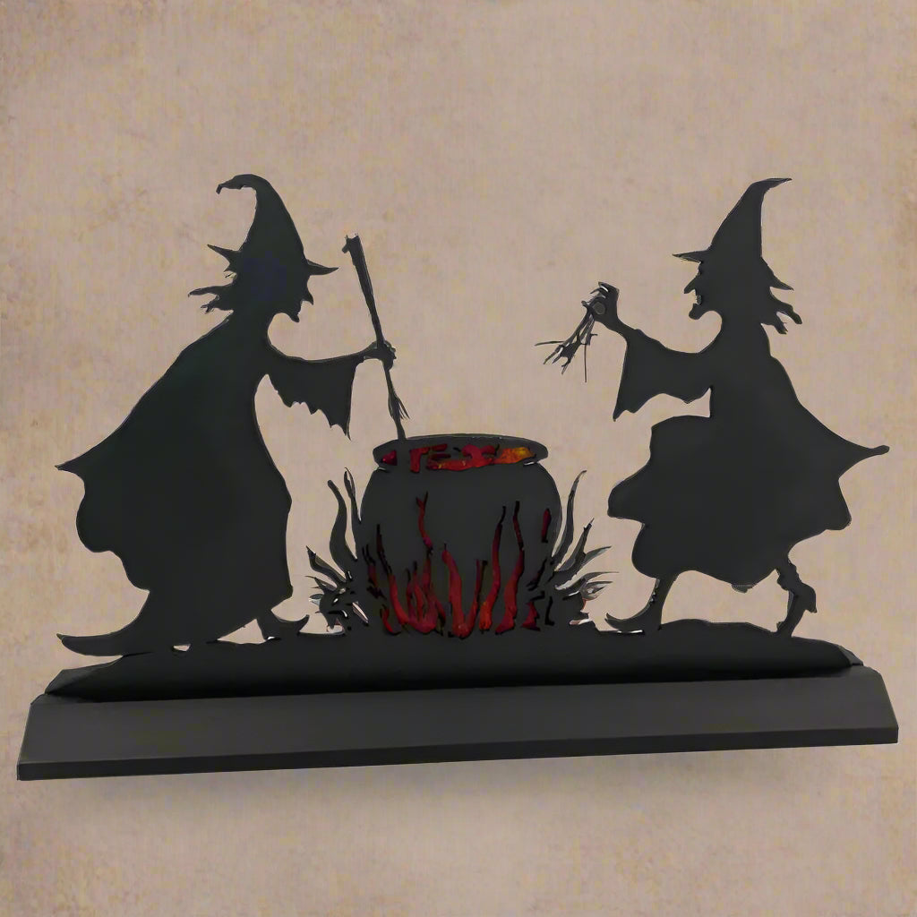 A silhouette of two witches with a cauldron in the center, with orange fire and witch's brew around it, set against a black background.